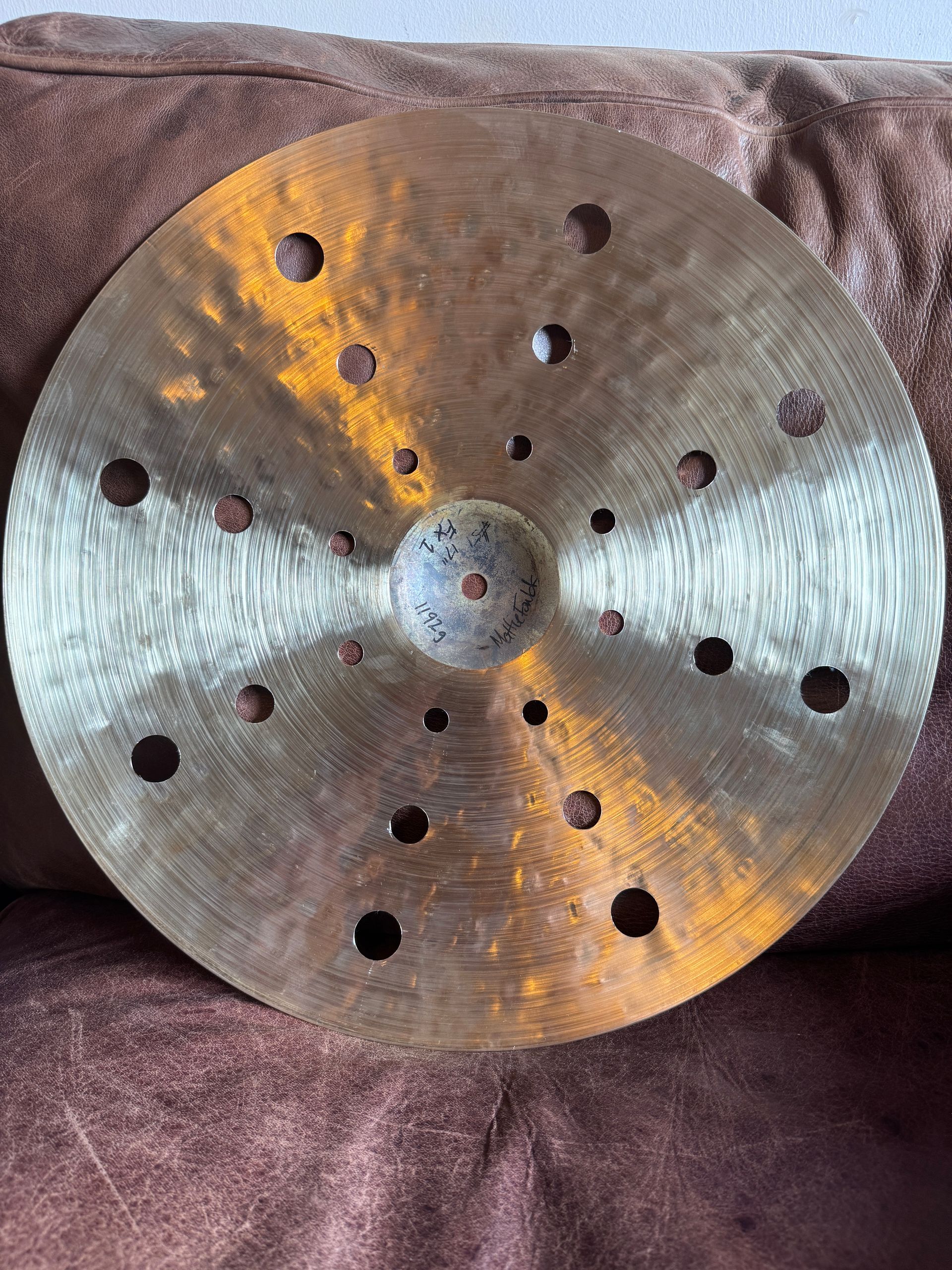 Gold-colored cymbal with holes, resting on a brown surface.