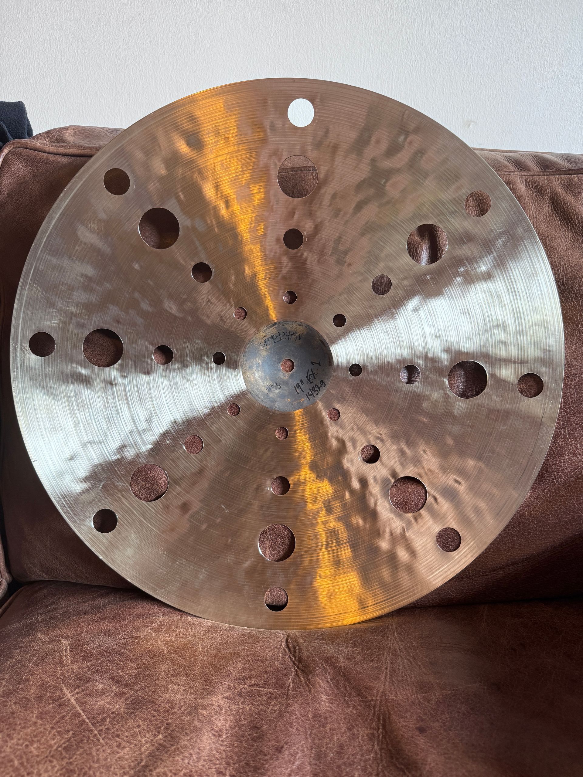 A bronze-colored cymbal with numerous holes, on a maroon couch.