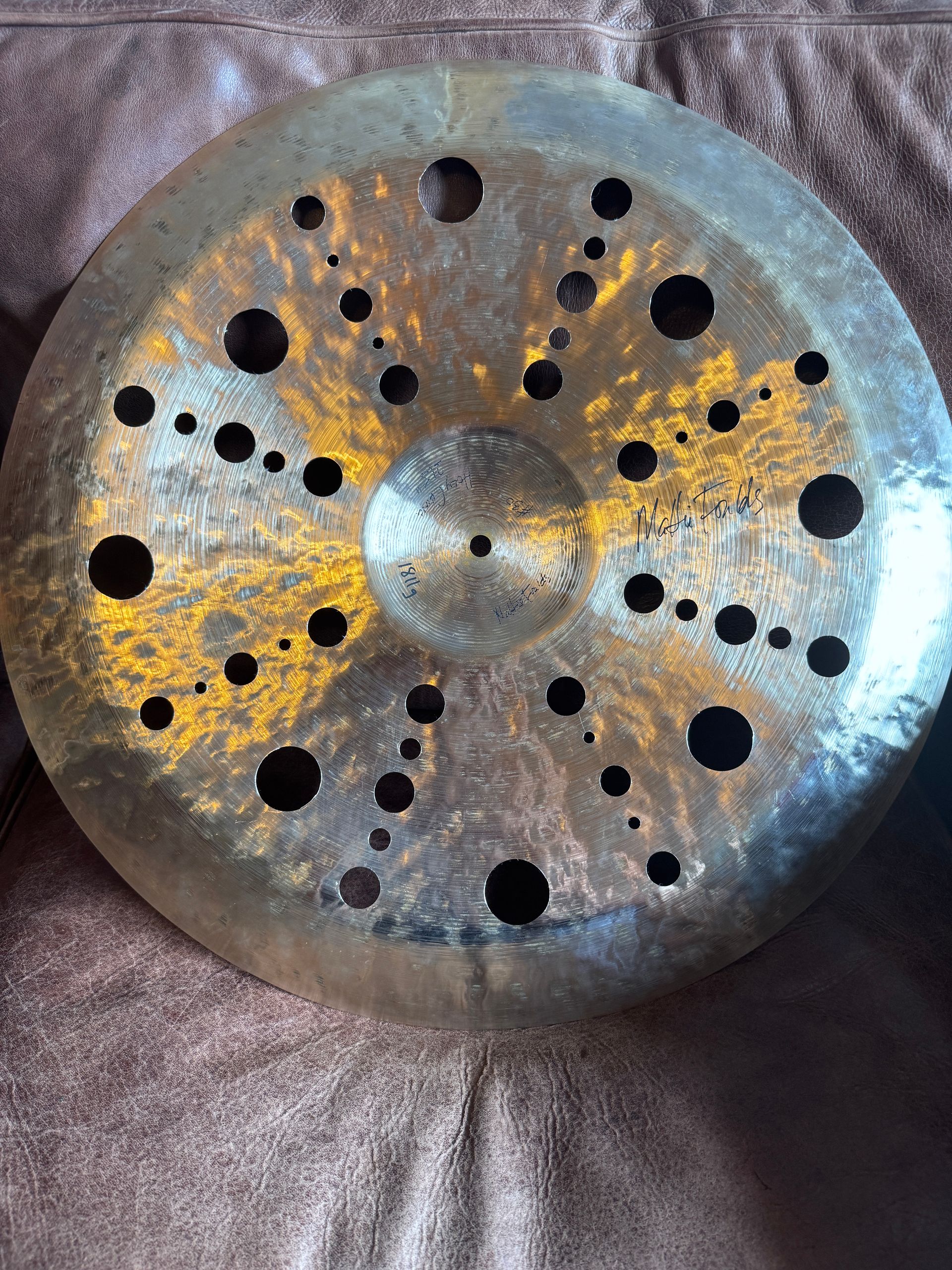 Bronze cymbal with many holes, resting on a brown surface.