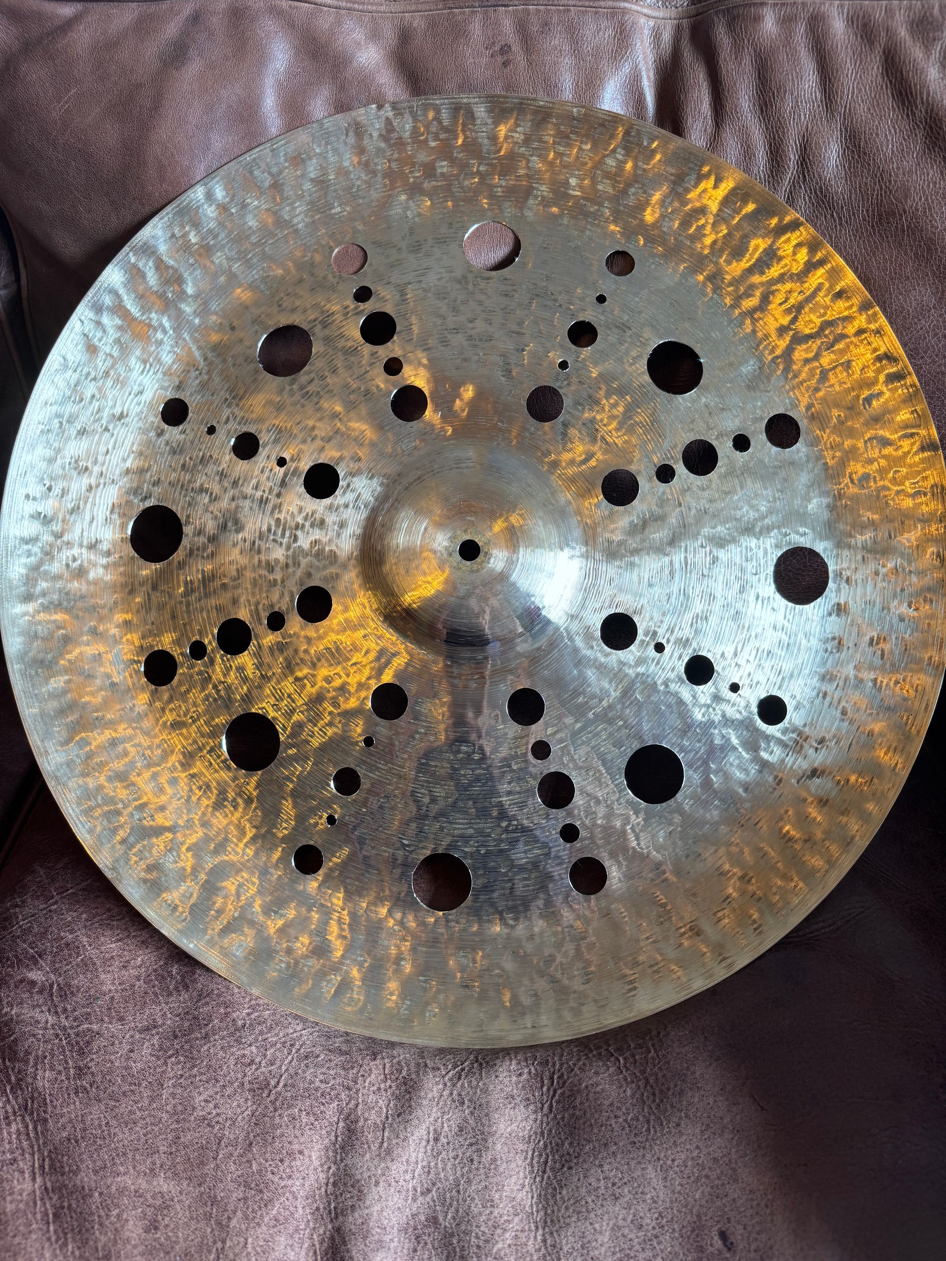Bronze cymbal with many holes, resting on a brown surface.
