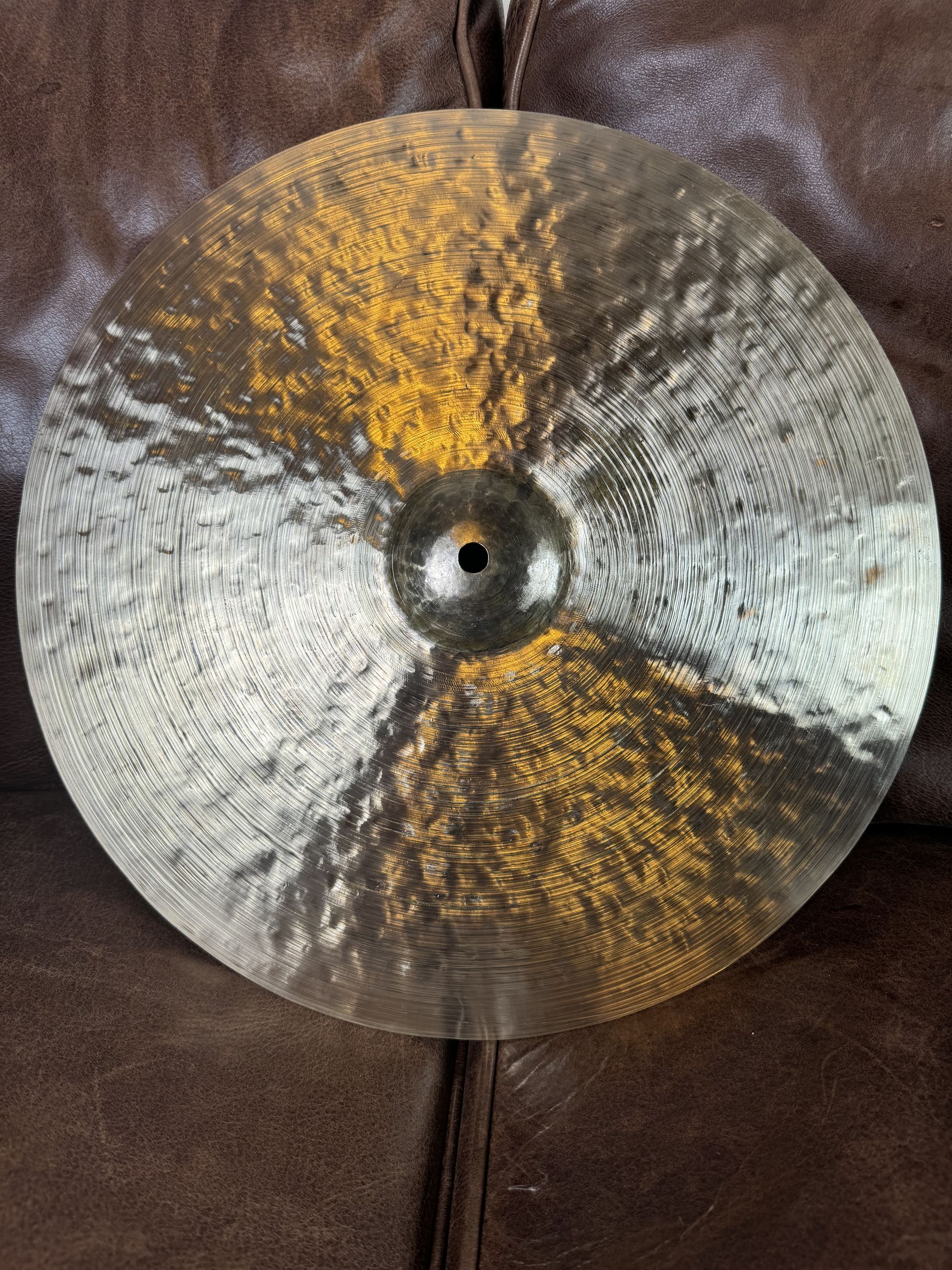 A round silver cymbal with gold splatter patterns on a brown surface.