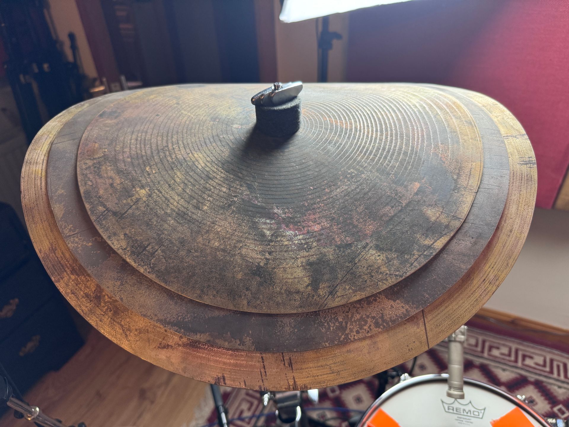 A round bronze gong with a central handle, seen indoors on a stand near a patterned rug.