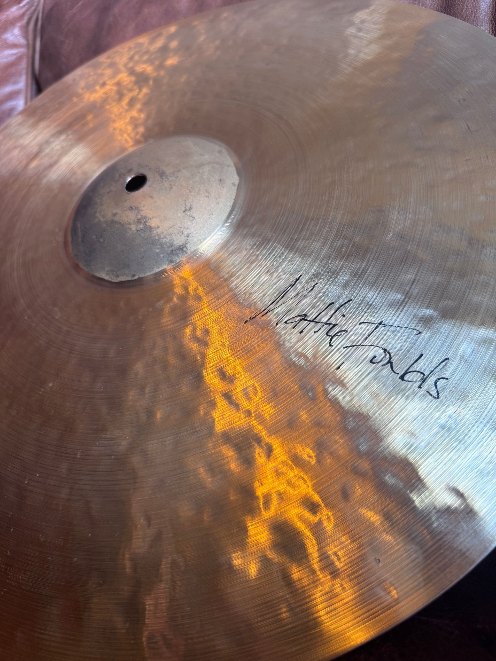Close-up of a hammered bronze cymbal with a central mounting hole and reflected orange light.