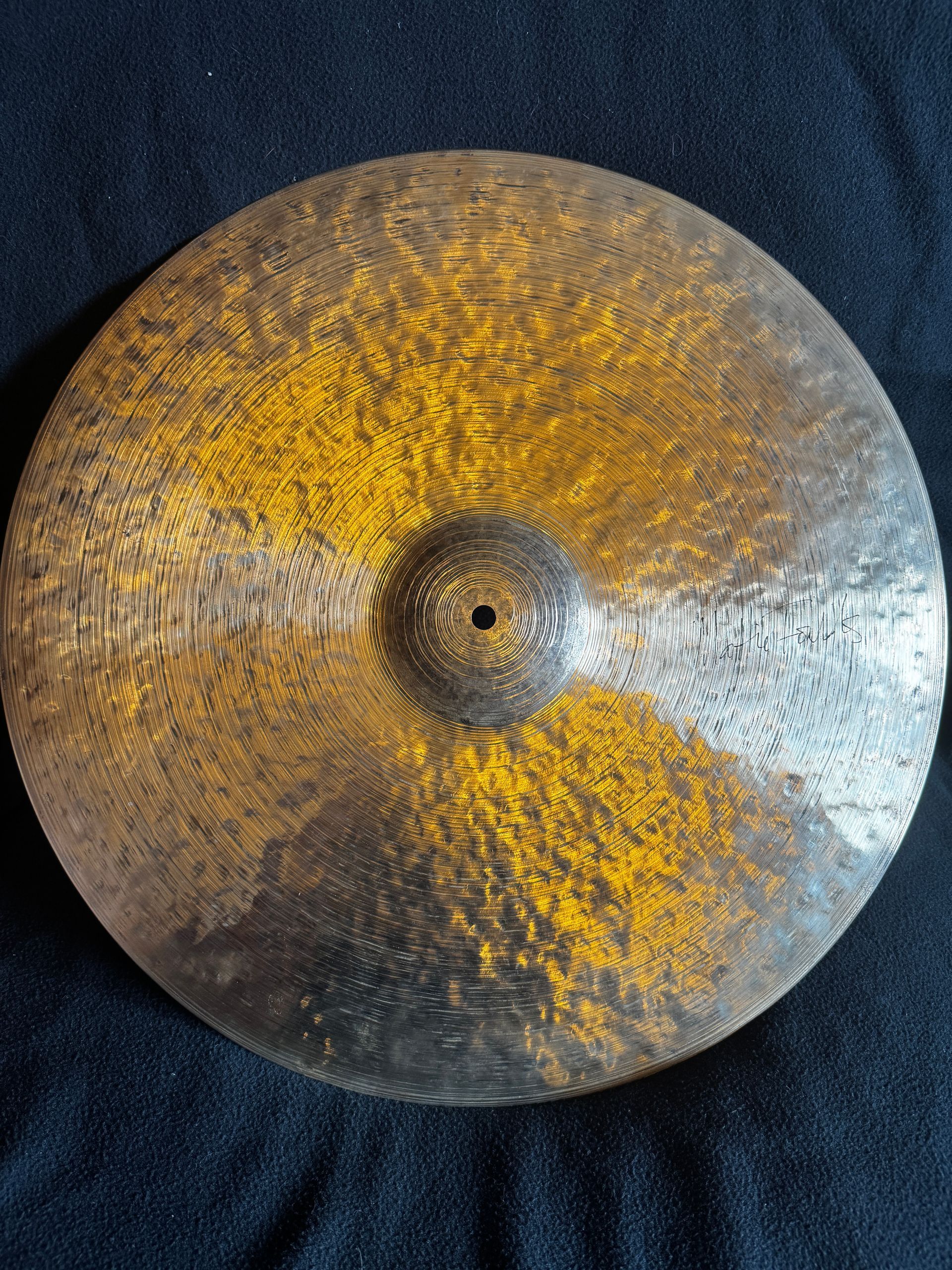 Close-up of a hammered metal cymbal with a golden center and silver edge on a dark fabric background