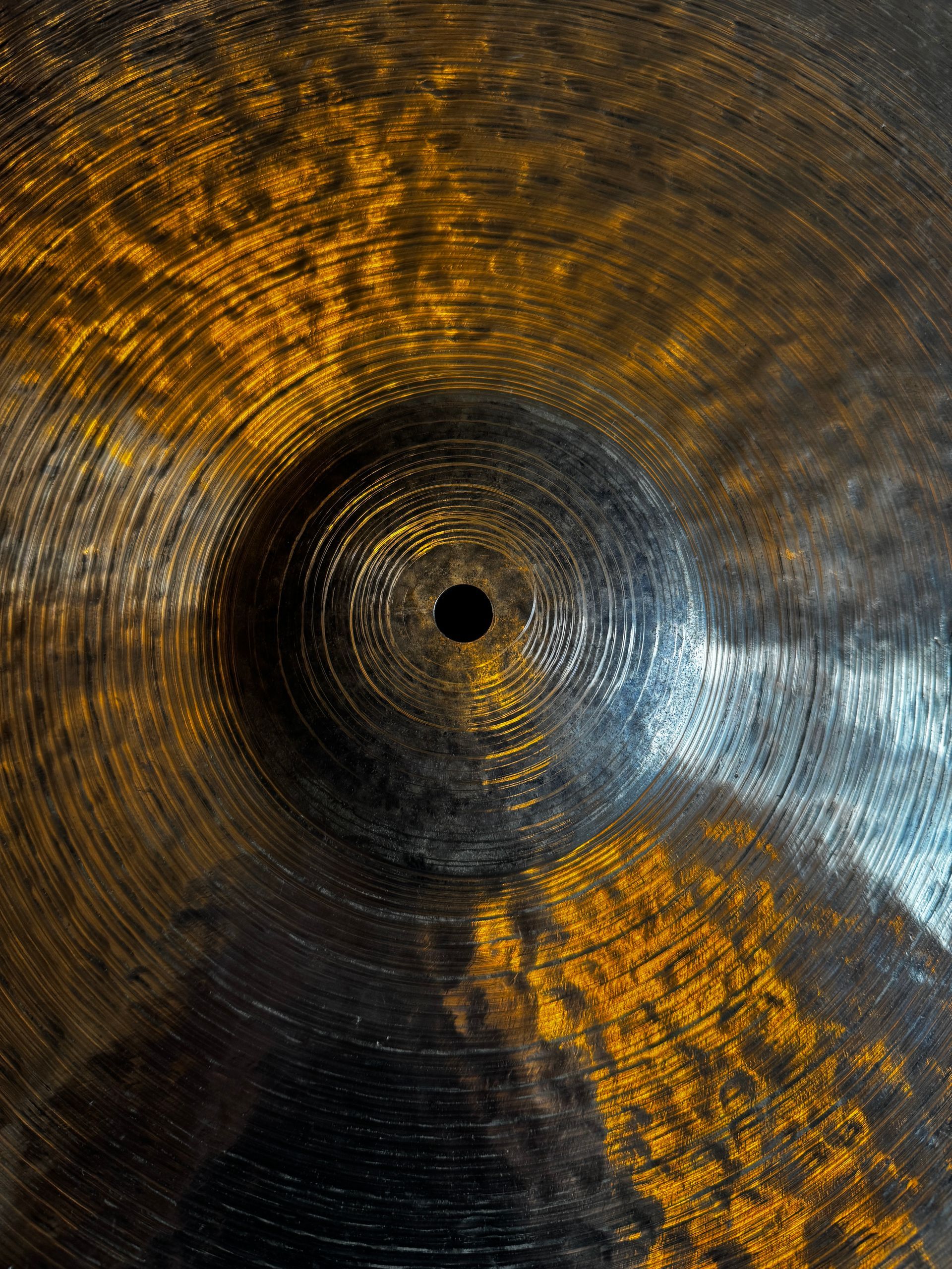 Close-up of a hammered metal cymbal with a golden center and silver edge on a dark fabric background