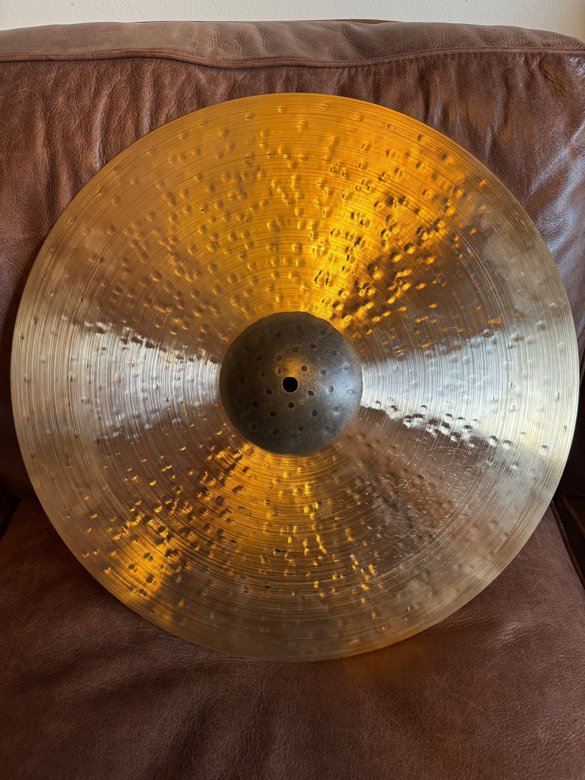 Large silver cymbal with a gold sheen resting on a brown couch.