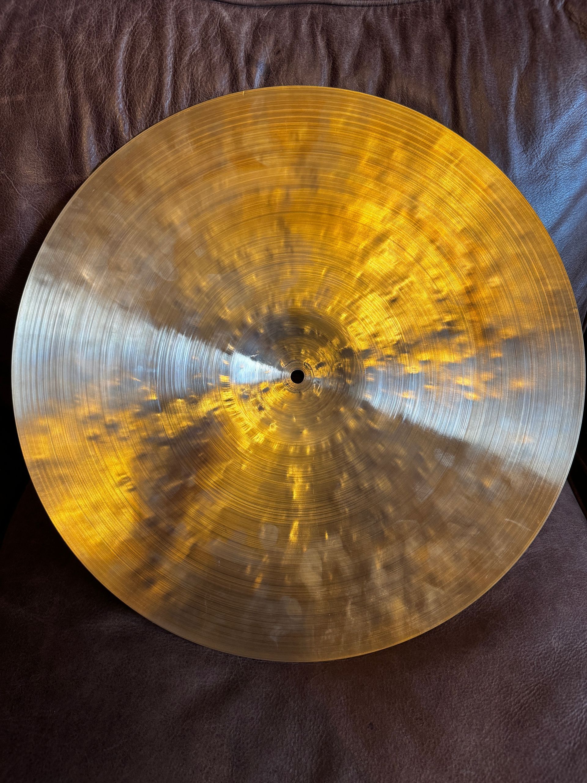 Large silver cymbal with a gold sheen resting on a brown couch.