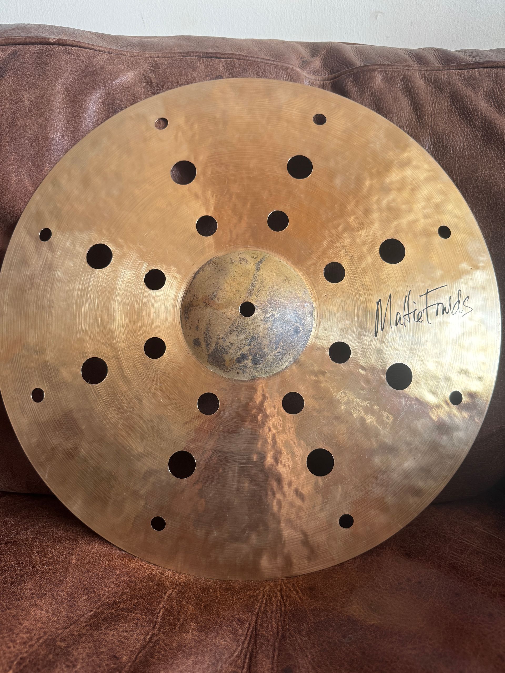 Round brass disc with many drilled holes and a raised center, resting on a brown fabric surface.