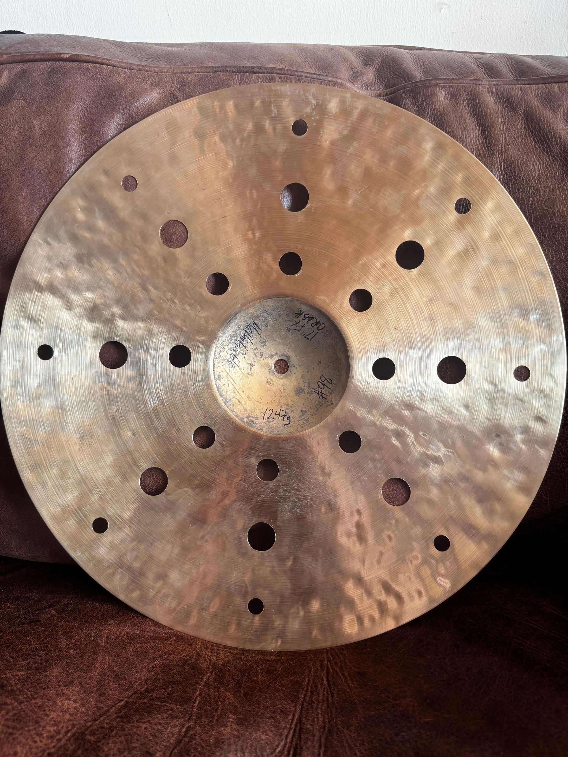 Round brass disc with many drilled holes and a raised center, resting on a brown fabric surface.