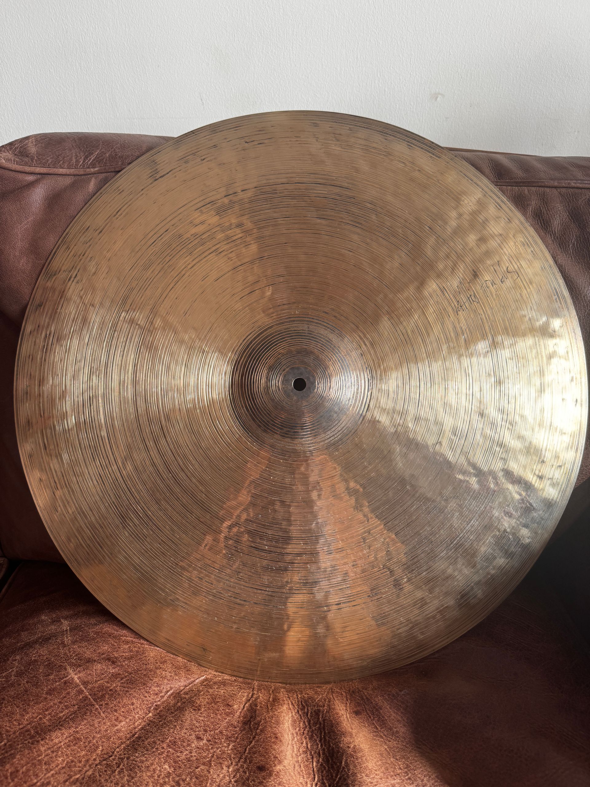Large round hammered brass gong resting against a brown fabric background.