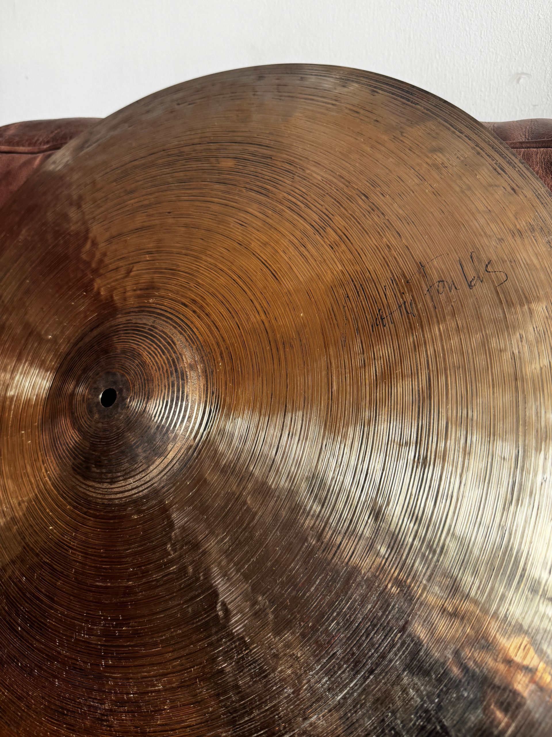 Large round hammered brass gong resting against a brown fabric background.