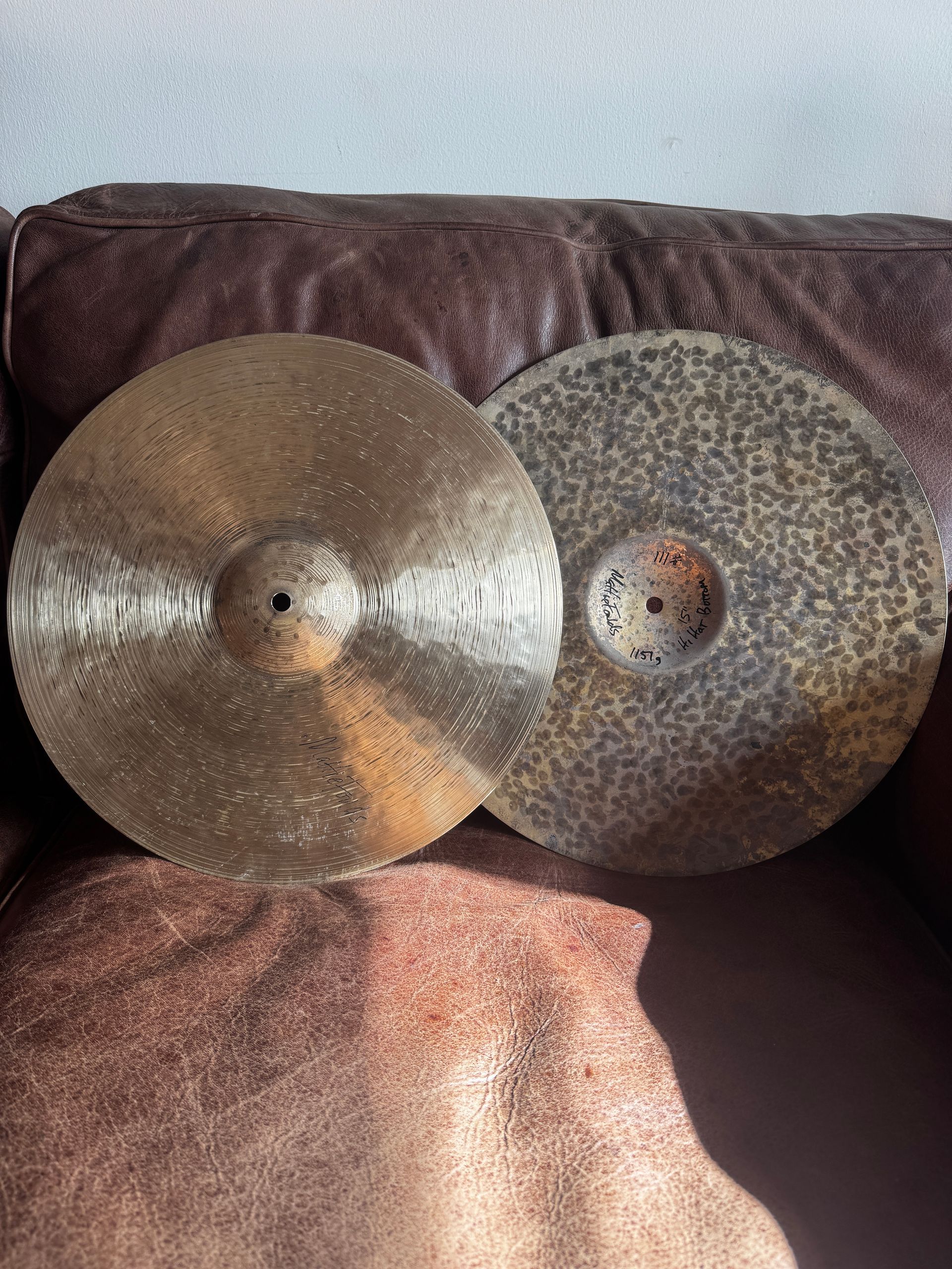 Two large metal cymbals leaning against a brown leather couch on a pink blanket.