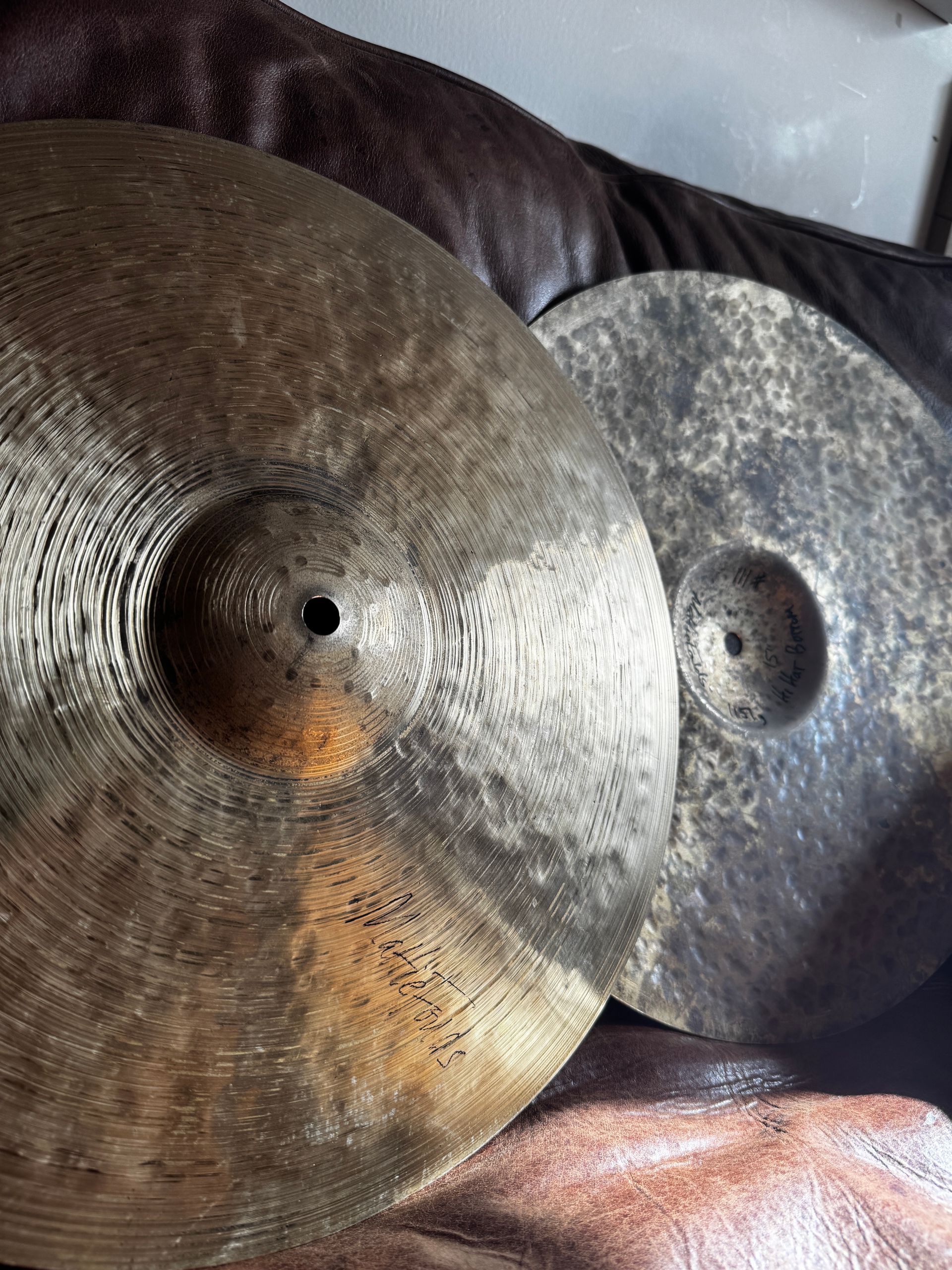 Two large metal cymbals leaning against a brown leather couch on a pink blanket.