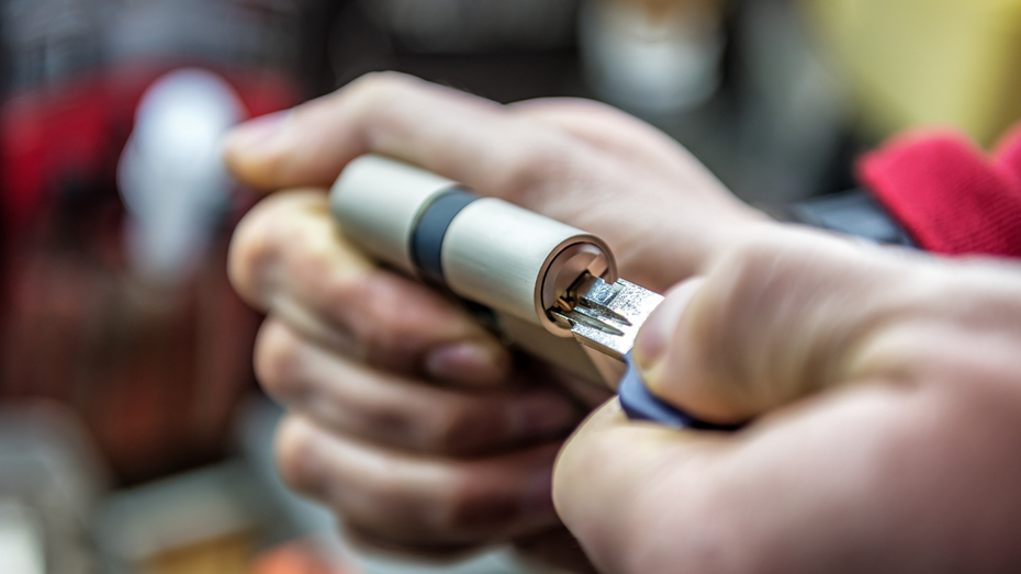 Hands inserting a key into a door lock cylinder.