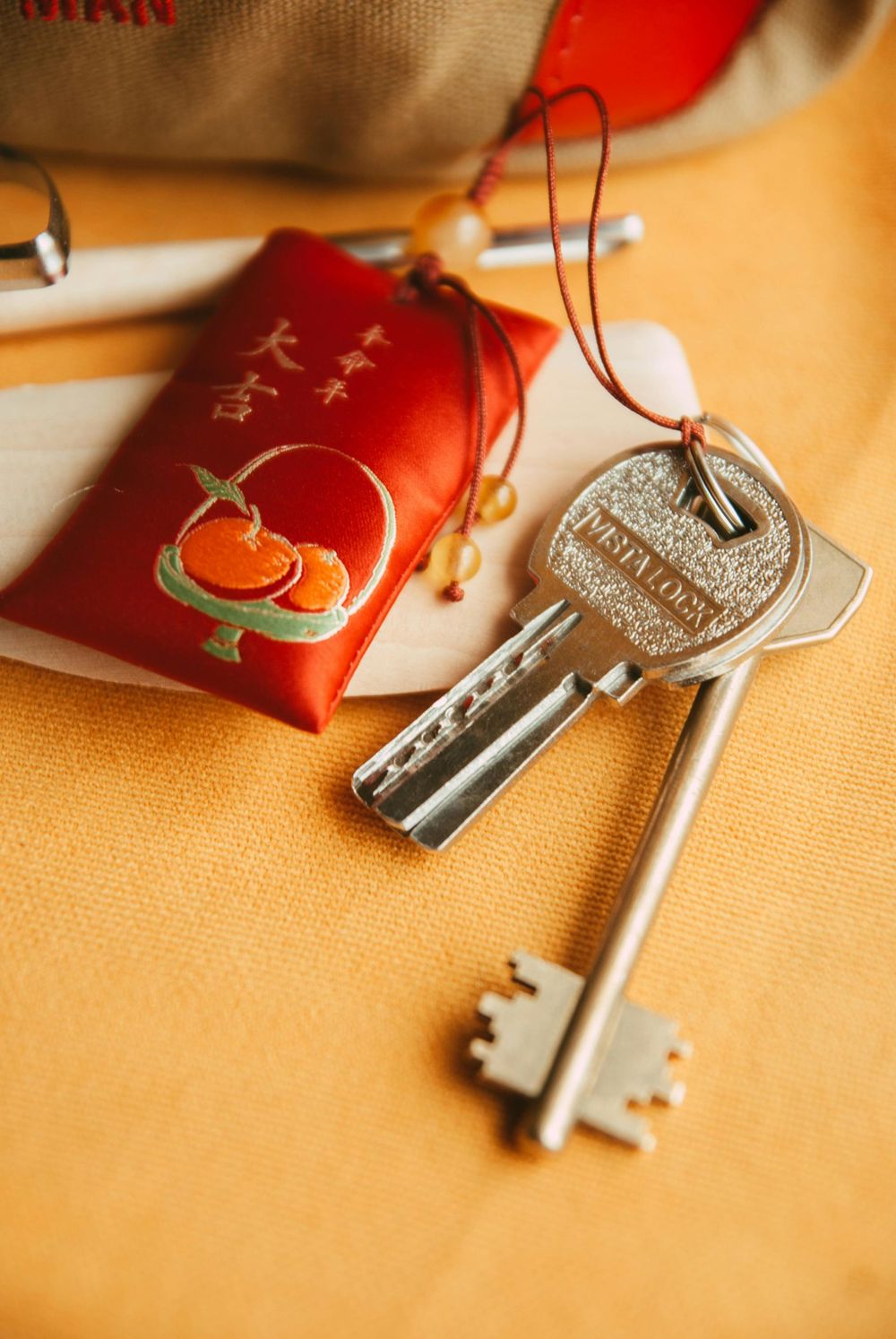 Keys with a red decorative pouch featuring oranges; on a yellow surface.