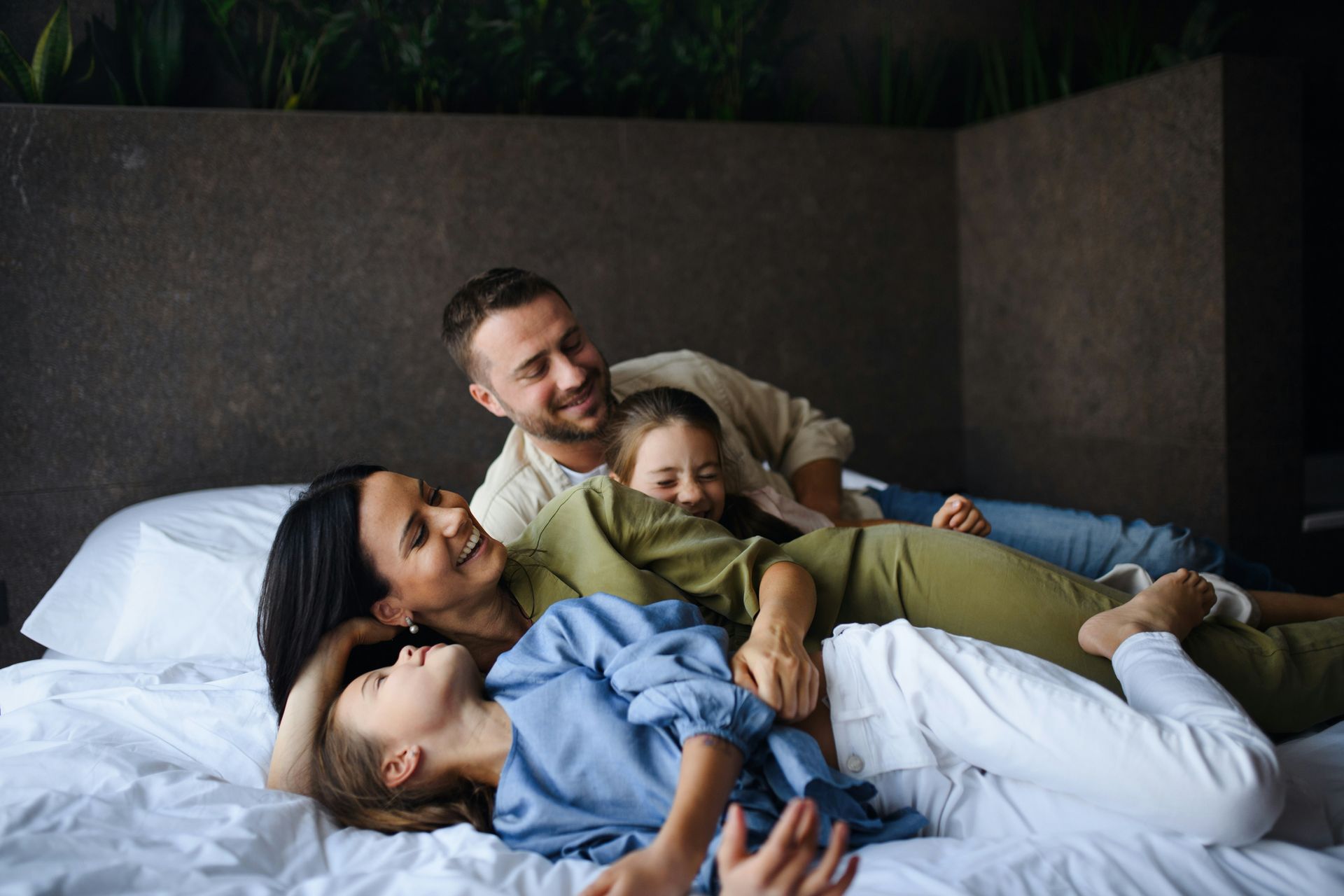 Family of four smiling and cuddling on a bed.