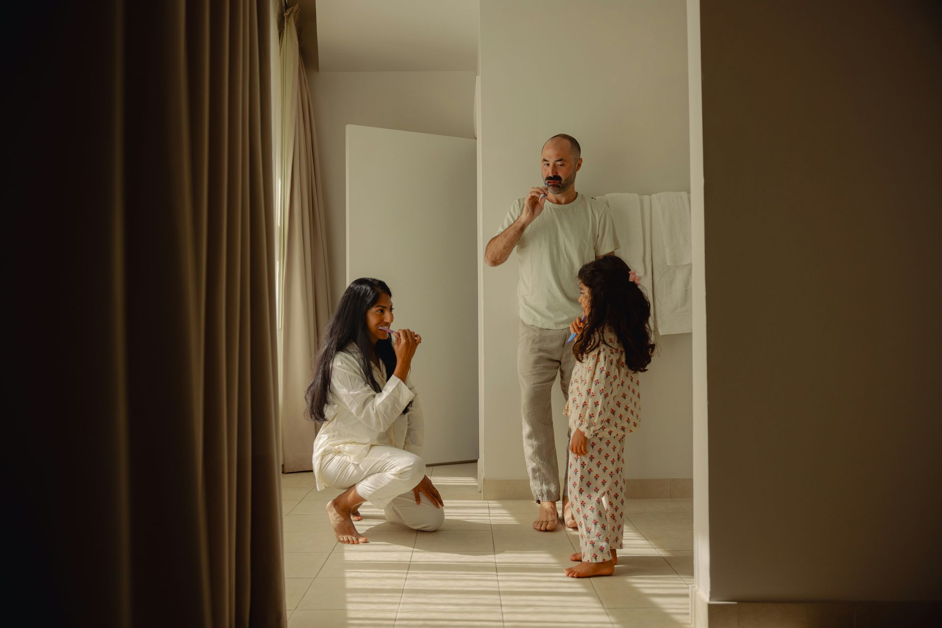 Family in pajamas brushing teeth in a bright bathroom.