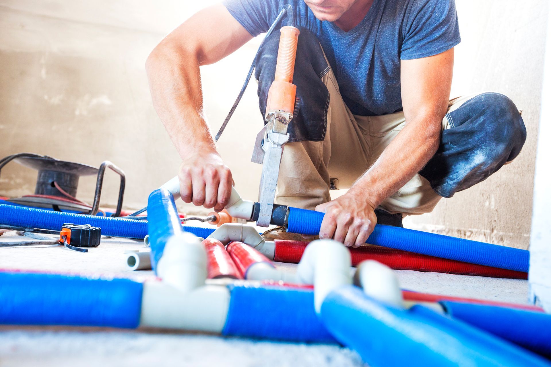Worker installing blue and white PVC pipes with a power drill on a floor.