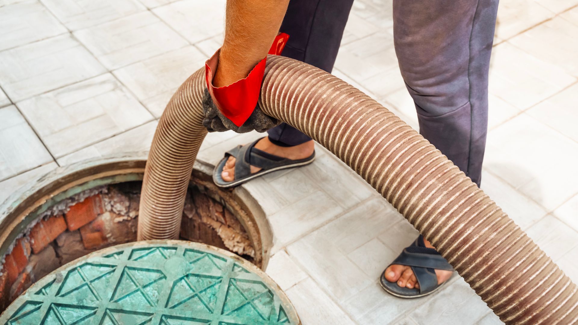 Worker using a hose to clean a manhole in tiled floor