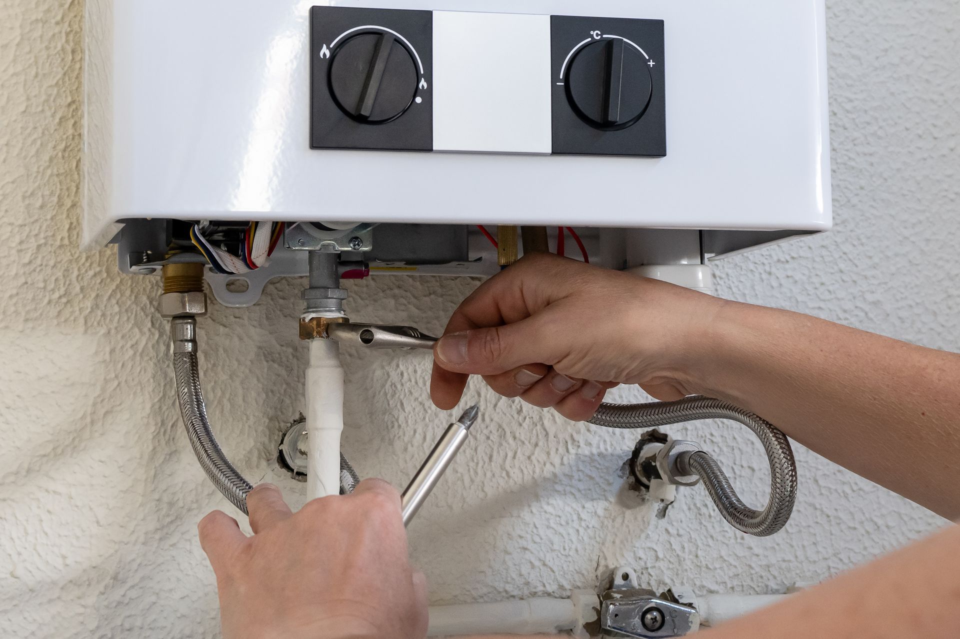 Hands using a wrench to repair pipes under a white wall-mounted water heater