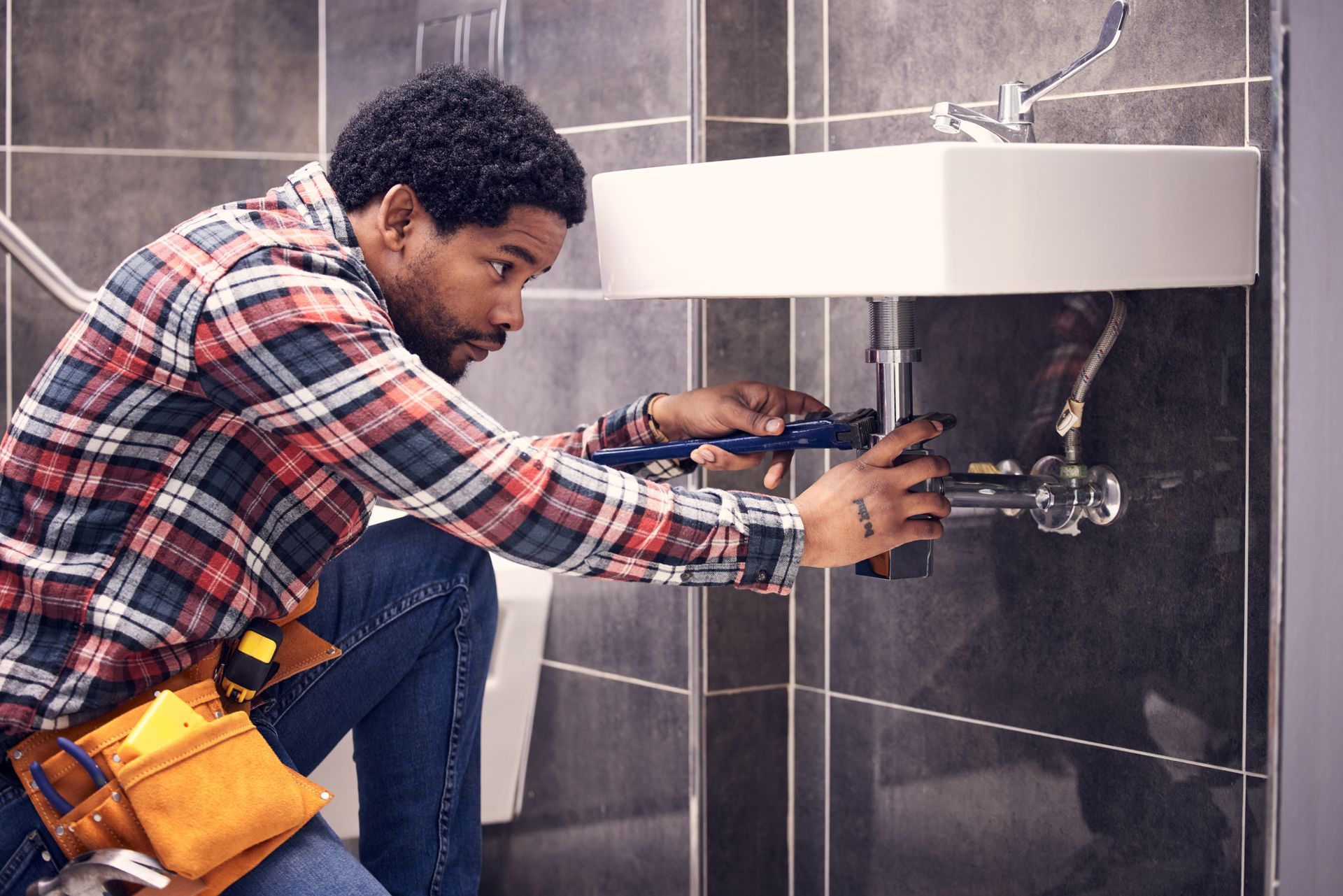 Plumber using tools to fix a sink pipe beneath a bathroom basin