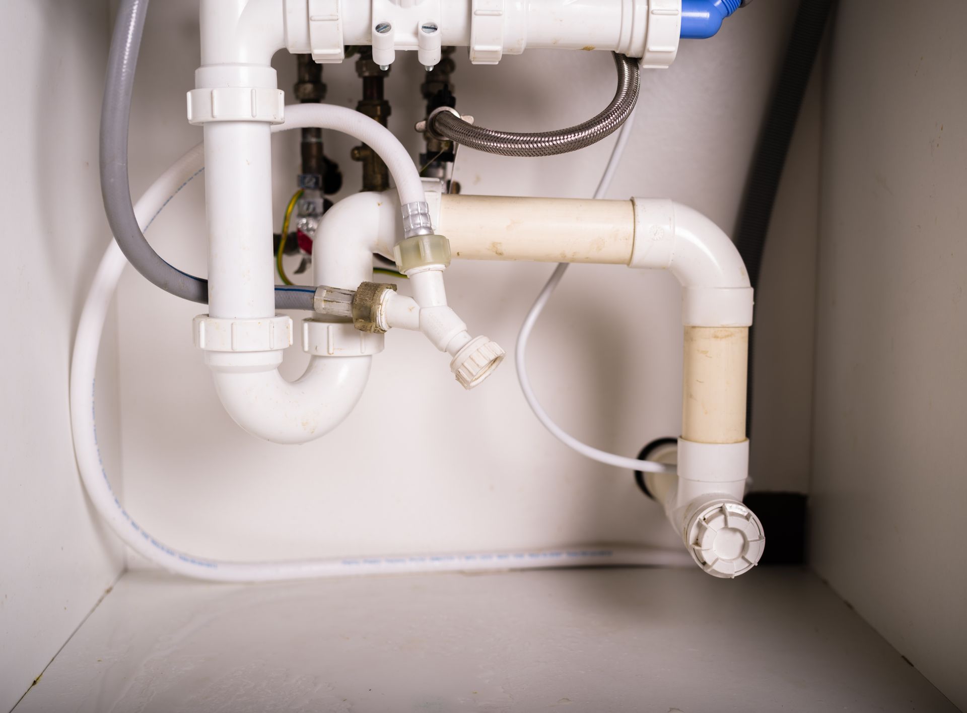 Under-sink plumbing with white PVC pipes and drain trap inside a cabinet