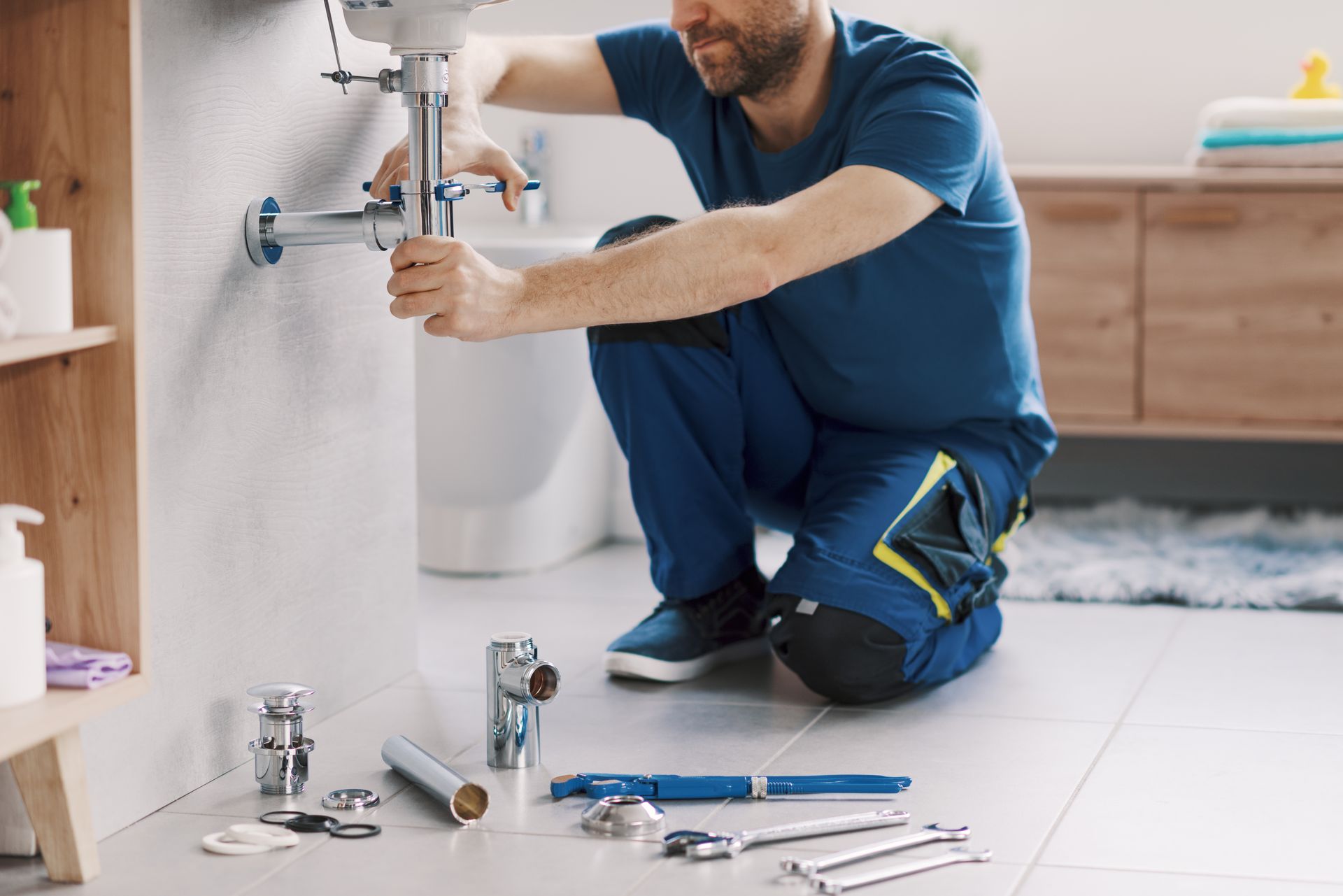 Plumber kneeling under a sink, tightening pipes with tools spread on the bathroom floor.