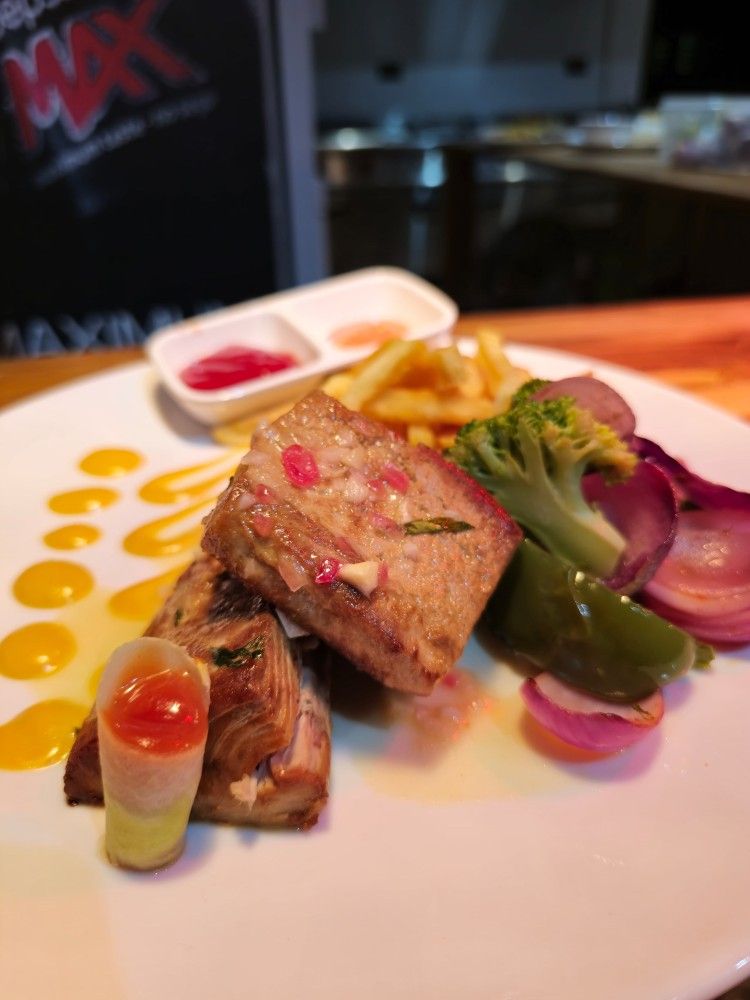 A white plate topped with meat and vegetables with a max logo in the background