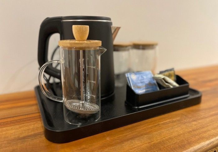 A black kettle and a glass pitcher are on a tray on a wooden table.