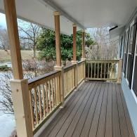 A wooden porch with a railing and support posts overlooks a grassy lawn on a cloudy day.
