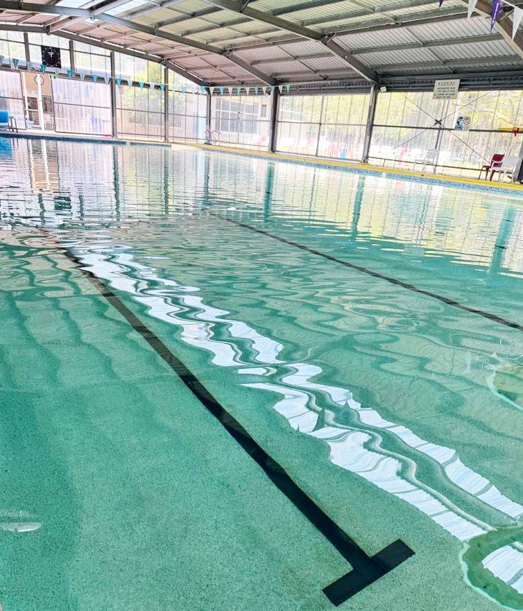 Indoor swimming pool with clear turquoise water and lane markings under a metal roof