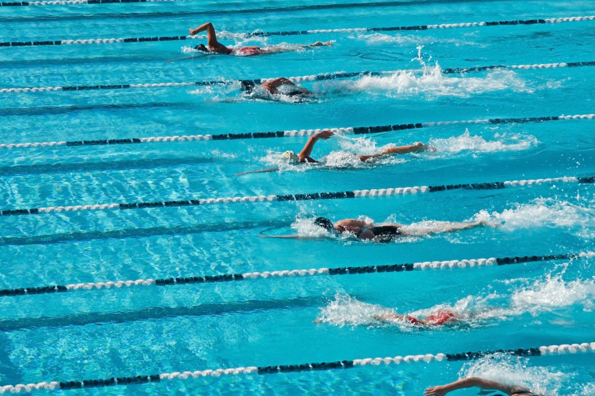 Swimmers racing in separate lanes of a bright blue outdoor pool — Valentine Swim School in Croudace Bay, NSW