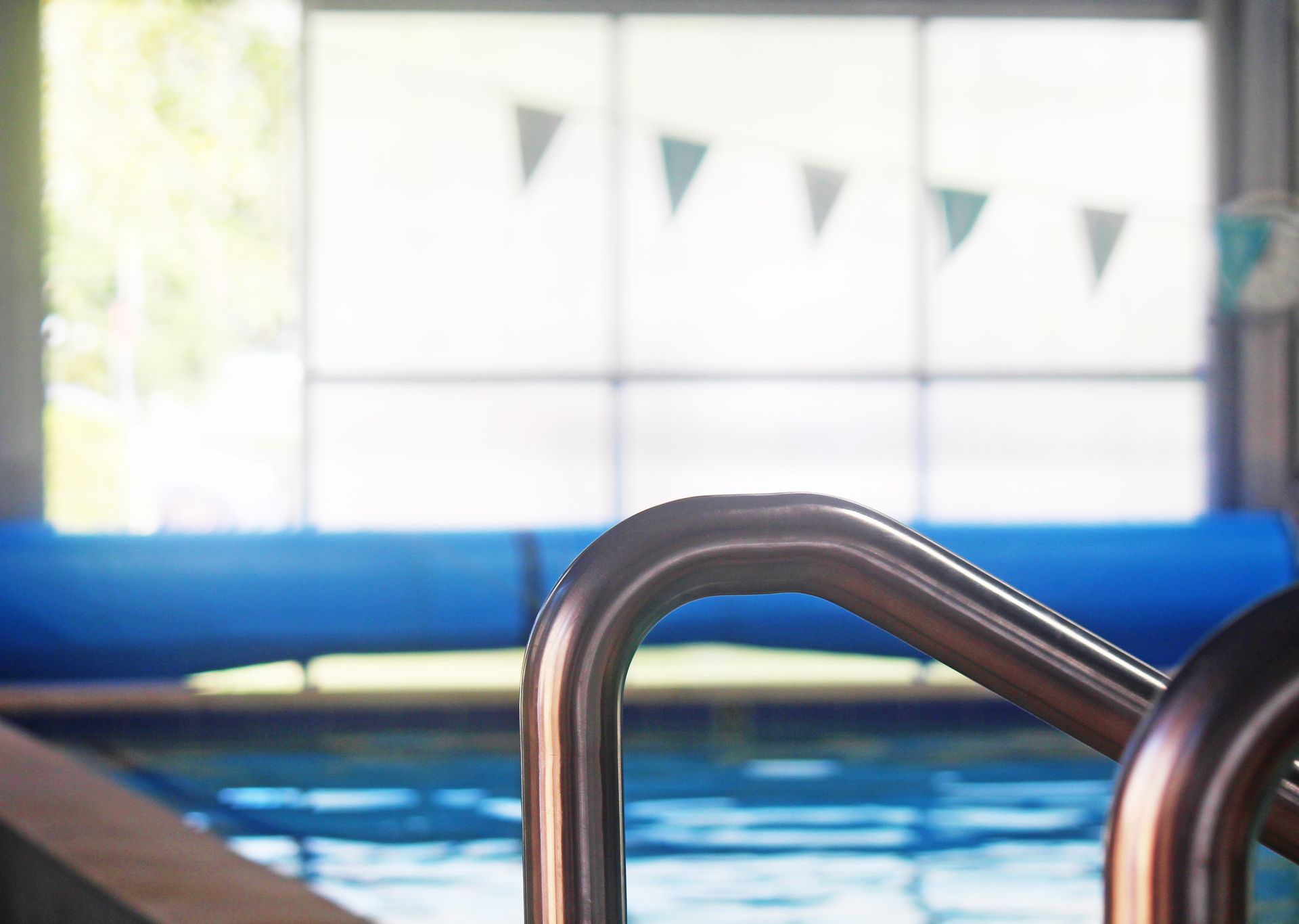 Indoor swimming pool with blue water and a metal handrail in the foreground