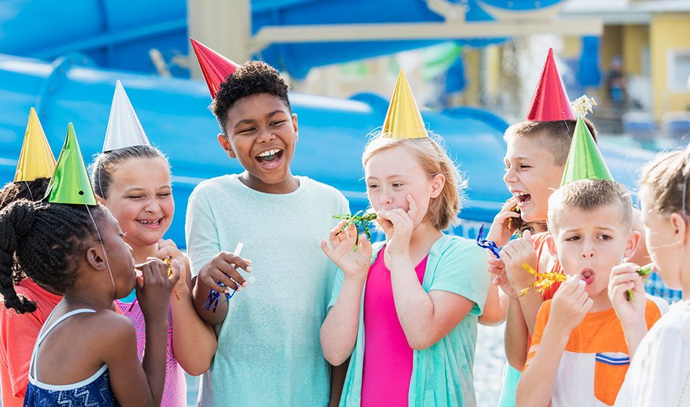 Children in colourful party hats blowing noisemakers at an outdoor birthday party — Valentine Swim School in Croudace Bay, NSW