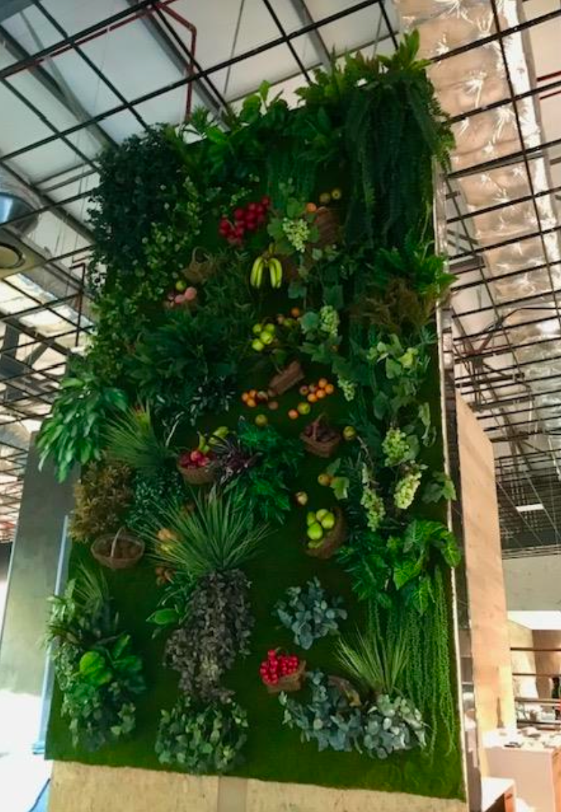 Mur végétal vertical avec plantes artificielles assorties, baies rouges et vertes et petits paniers suspendus.