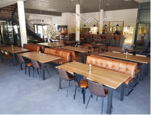 Intérieur de restaurant avec tables, sièges, bar et escalier. Couleurs marron et gris avec éclairage lumineux.