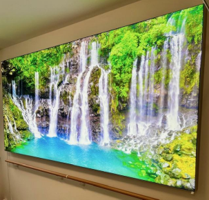 Grand écran numérique affichant une cascade vibrante, fixé au mur. Eau turquoise, arbres verts.