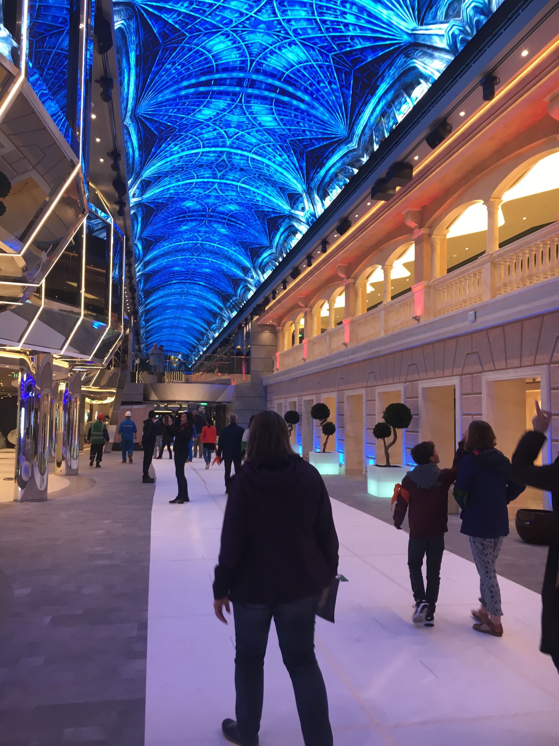 Passerelle intérieure avec des gens sous un plafond LED bleu et orné ; des magasins bordent le côté droit.