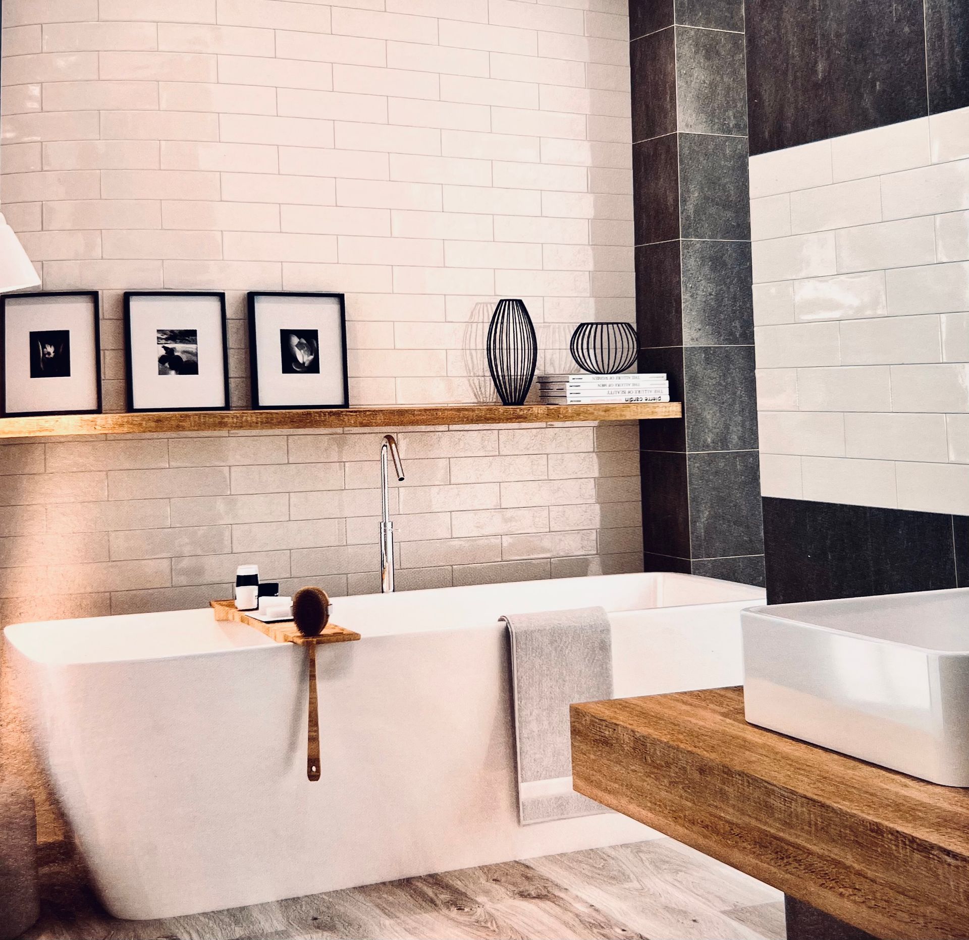 Salle de bain moderne avec baignoire blanche, étagère en bois et carrelage noir et blanc.