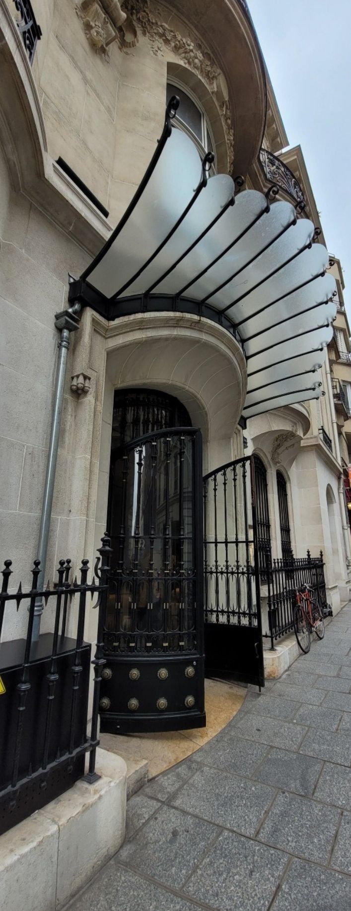 Entrée ornée avec un auvent en verre et un portail en métal noir.