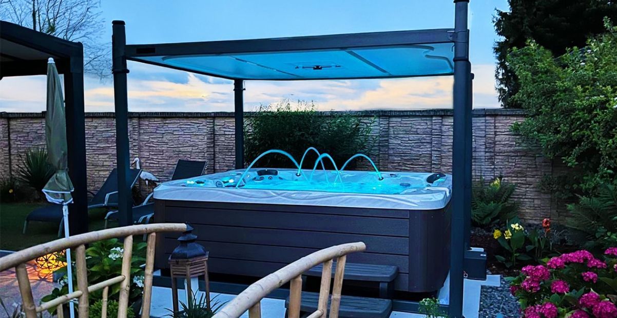 Bain à remous avec jets d'eau sous une pergola dans une cour arrière, en fin de soirée.