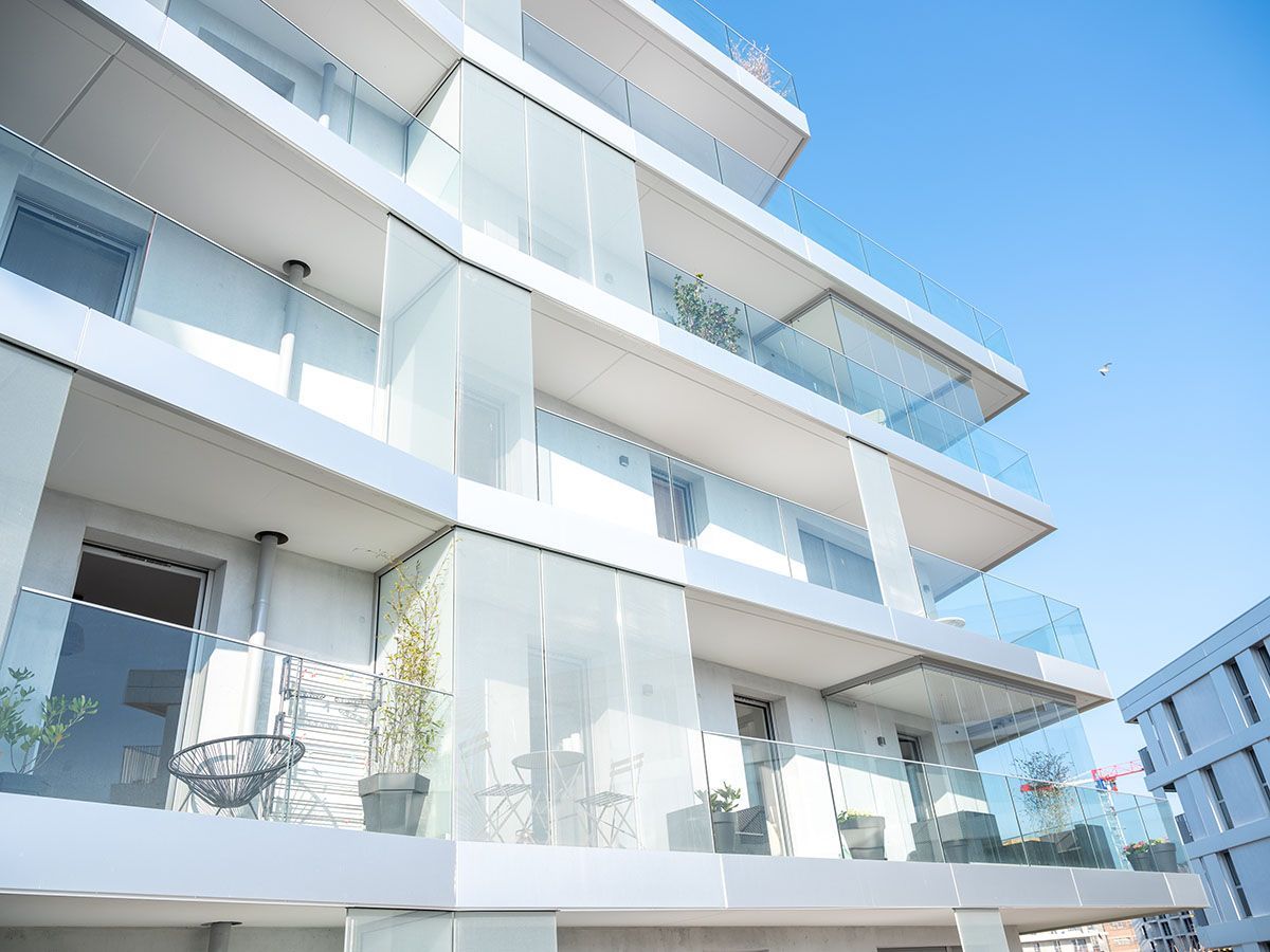 Bâtiment blanc moderne avec balcons en verre contre un ciel bleu clair.
