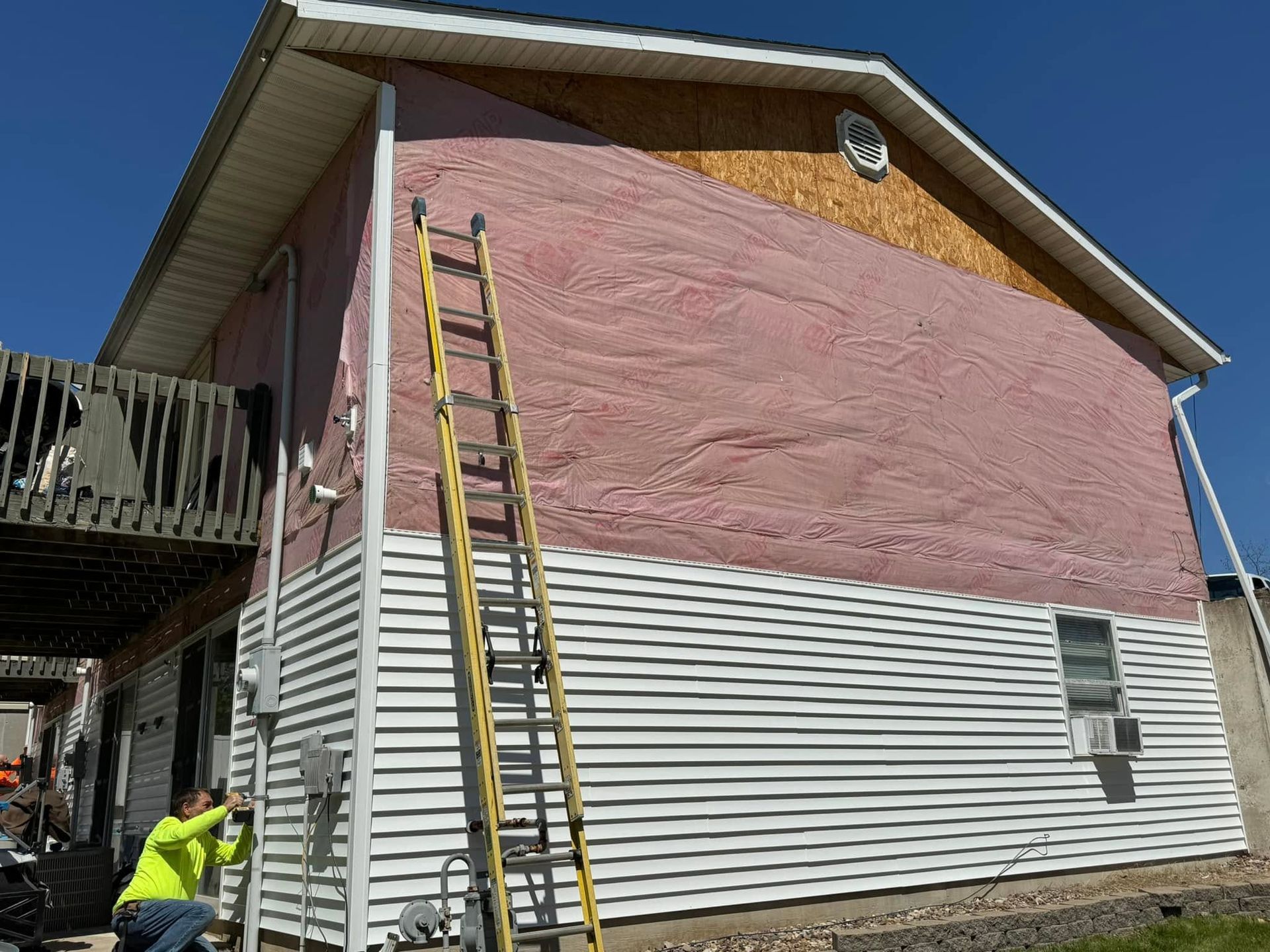 Workers painting a pink exterior wall of a house with a ladder nearby