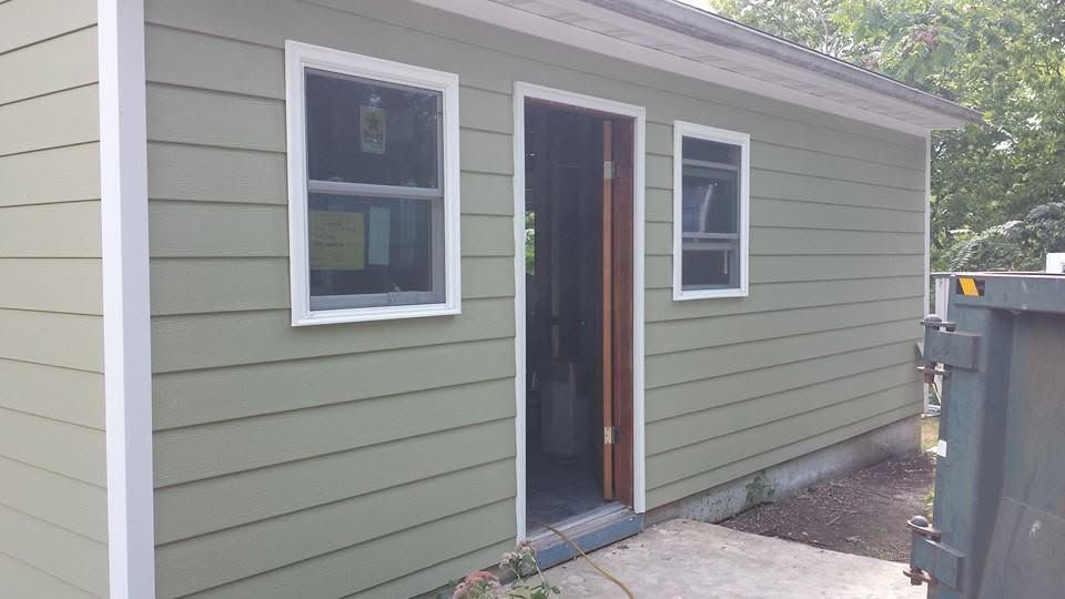 Back door of a house with green siding and white trim, beside a dumpster.