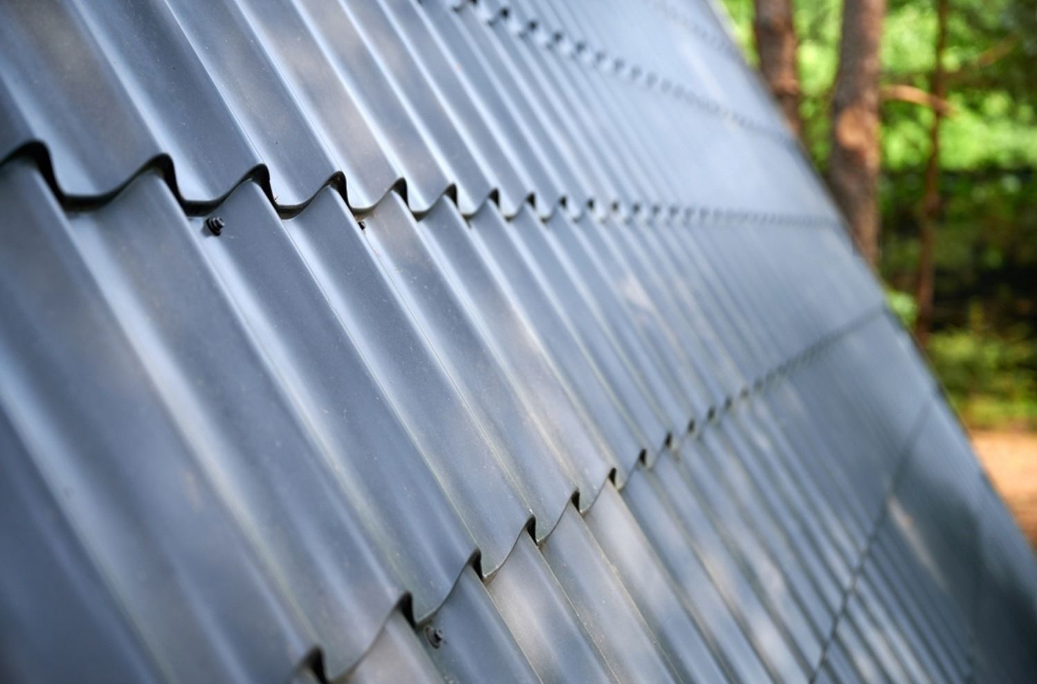 Close-up of a gray corrugated metal roof with a blurred green background