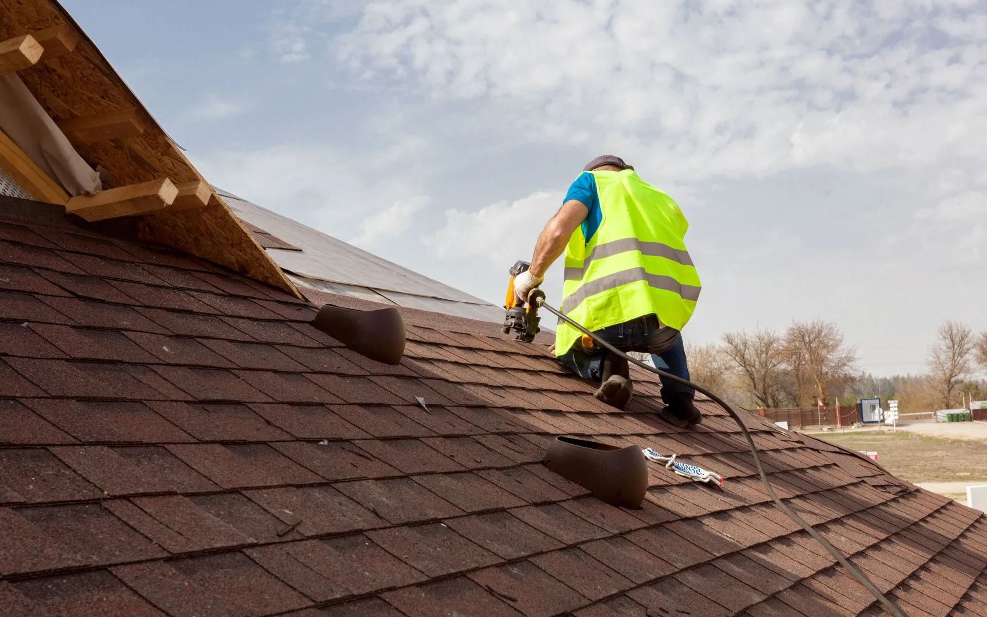 Worker in a neon safety vest installing roof shingles on a house