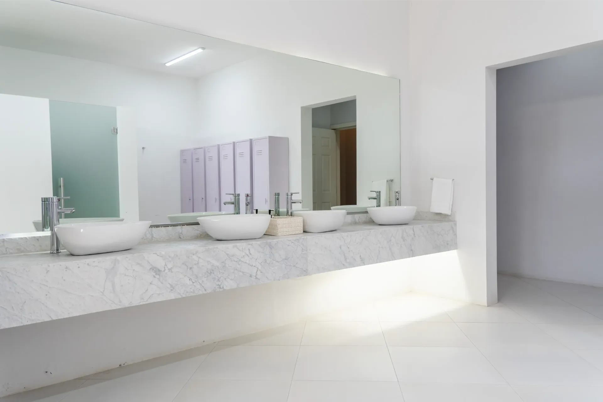 Baño moderno blanco con dos lavabos, un espejo grande y toallas color lavanda en un interior minimalista y luminoso