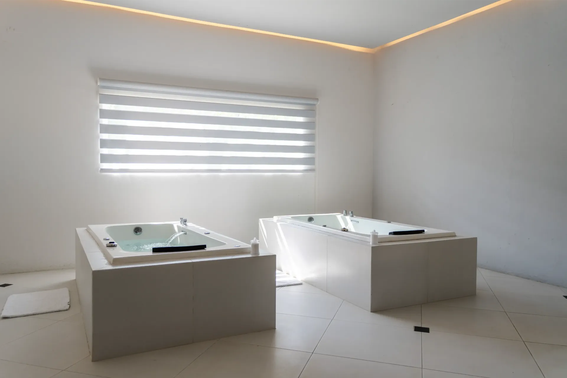 Baño luminoso con dos bañeras blancas, una ventana e iluminación empotrada en el techo.