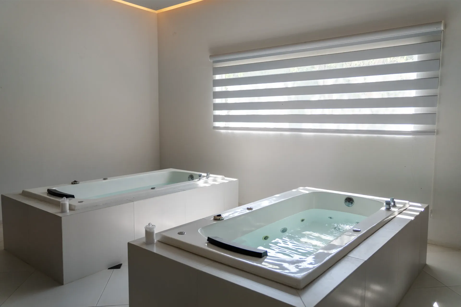 Moderna sala de spa con dos jacuzzis blancos y una ventana con persianas a rayas