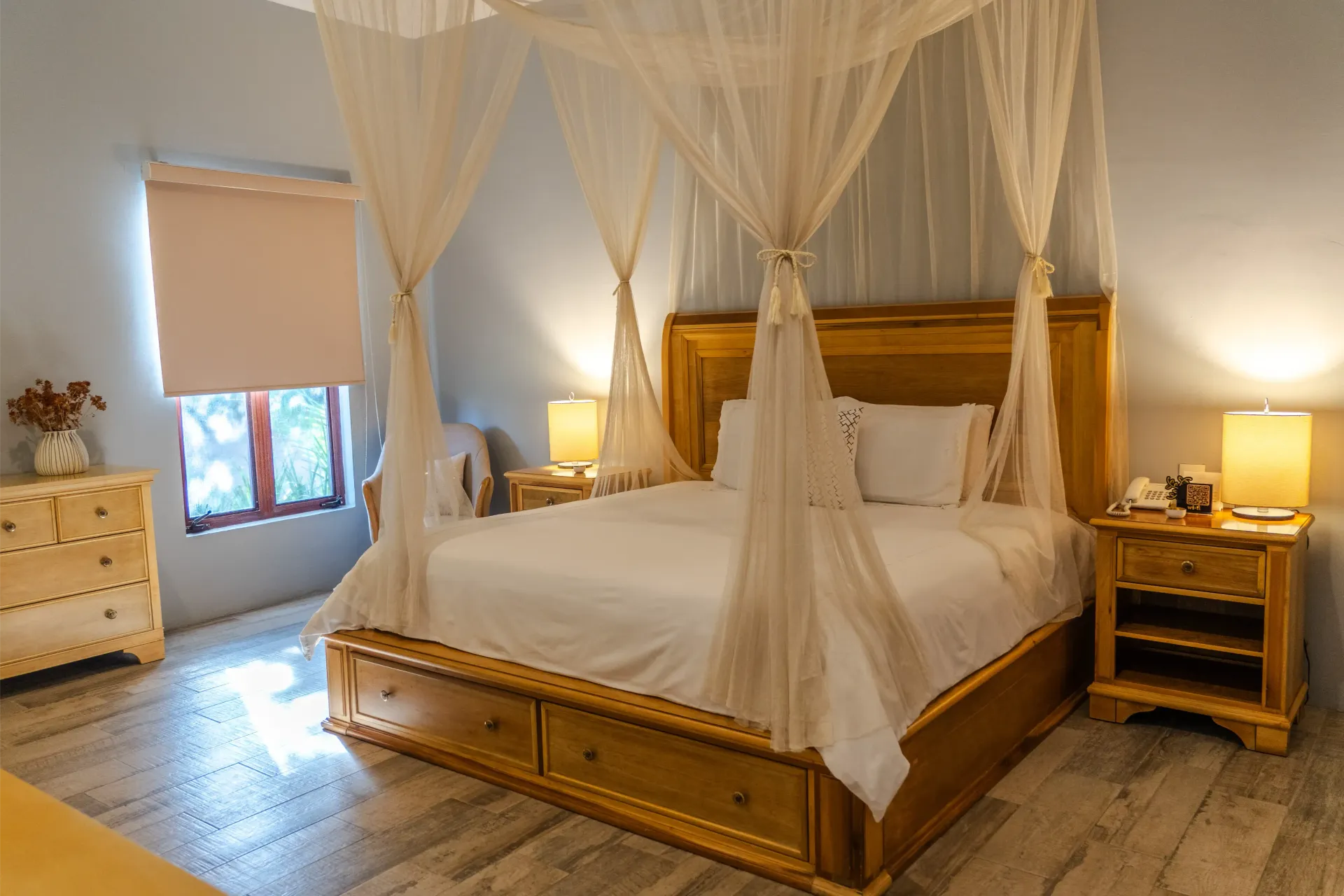 Dormitorio con una cama de madera con dosel, cortinas blancas vaporosas y cálidas lámparas de noche